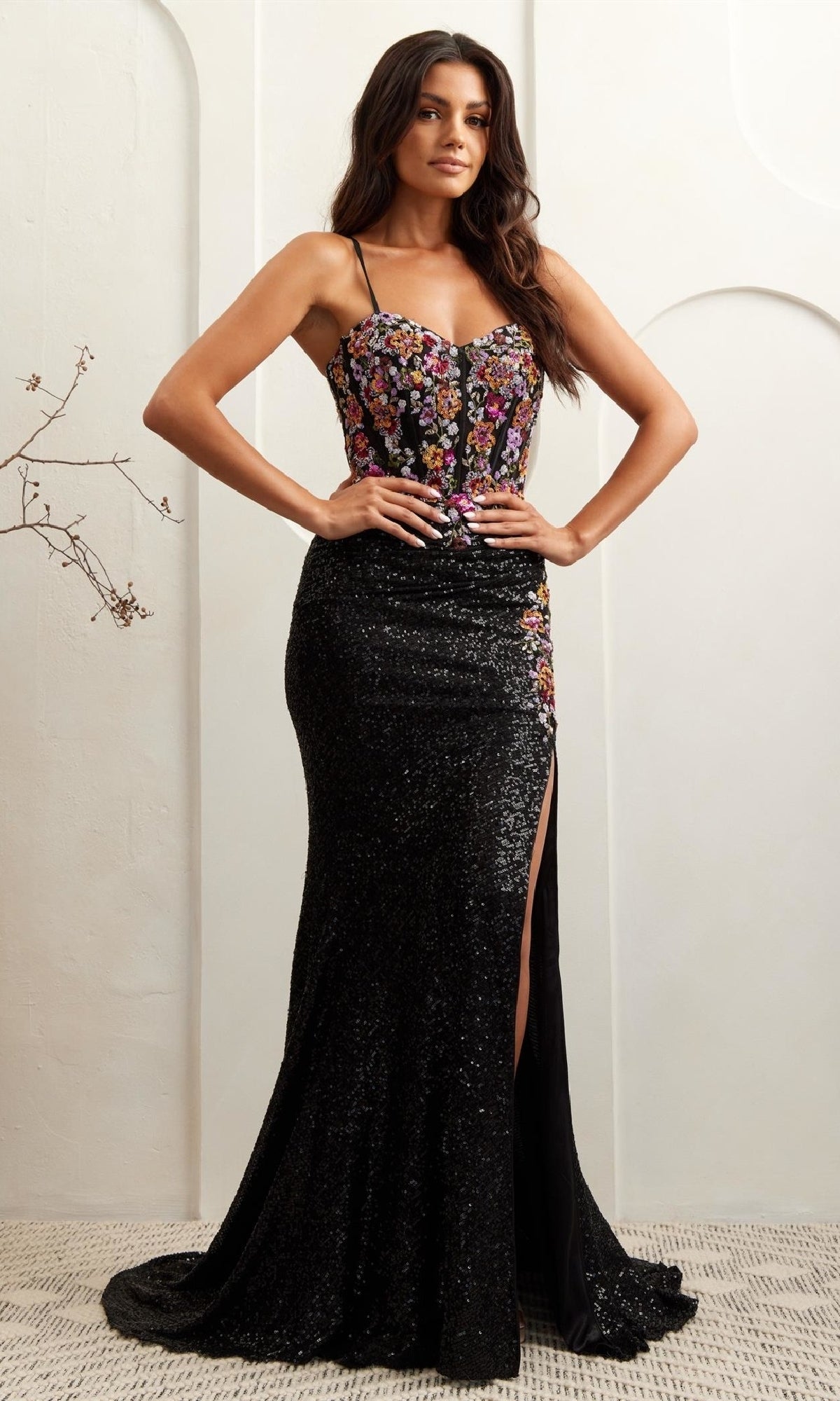 A woman wears the Amelia Couture 7061 Multicolored Sequin Prom Gown, featuring a floor-length skirt with a thigh-high slit and a fitted bodice with thin straps.